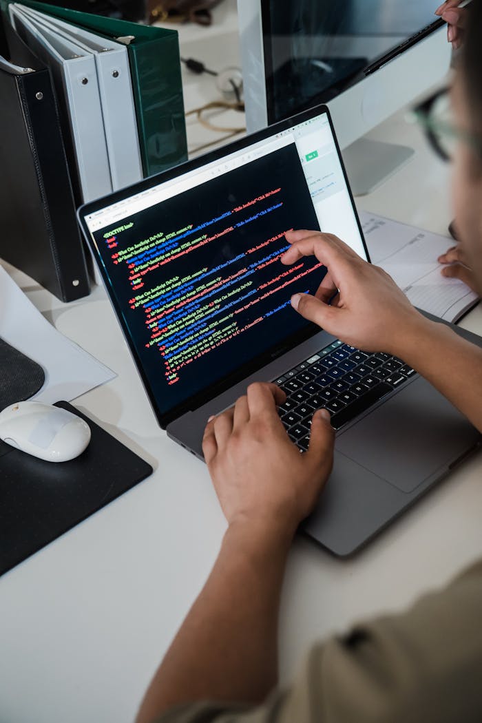 services-02 Close-up of a programmer pointing at a colorful code script on a laptop in an office setting.